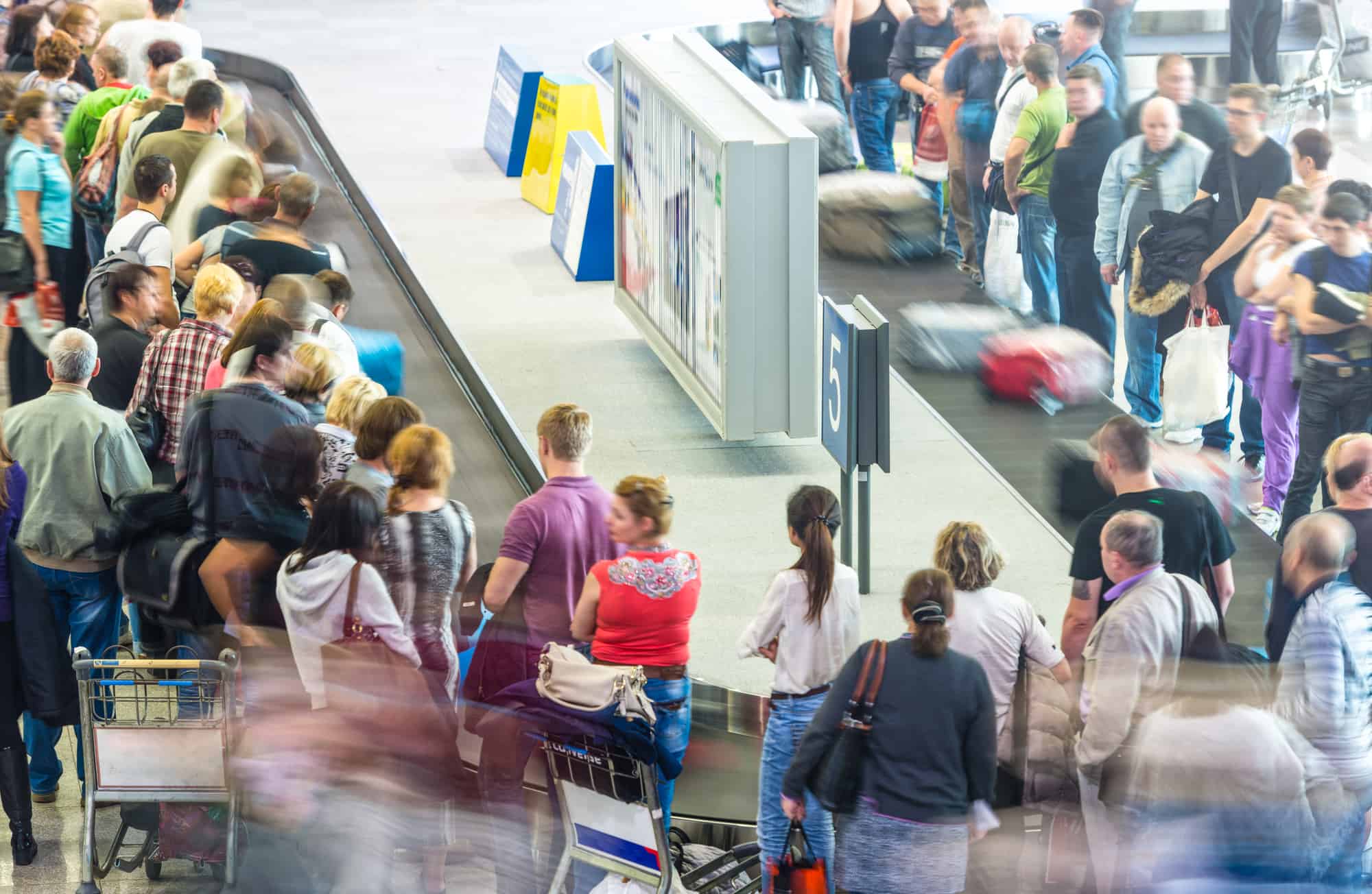 A lot of people waiting for their luggage at a luggage track